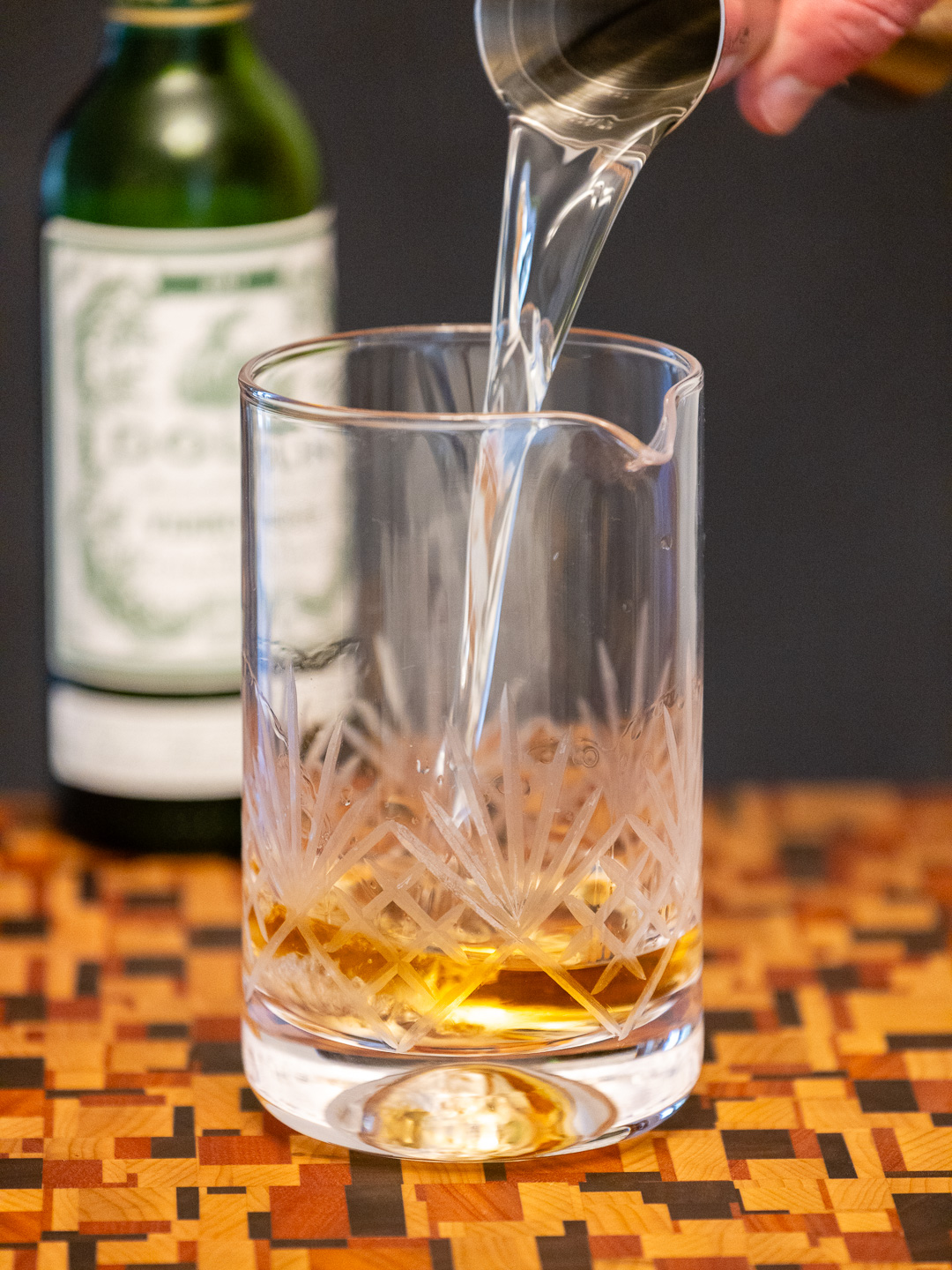Pouring dry vermouth into a mixing glass