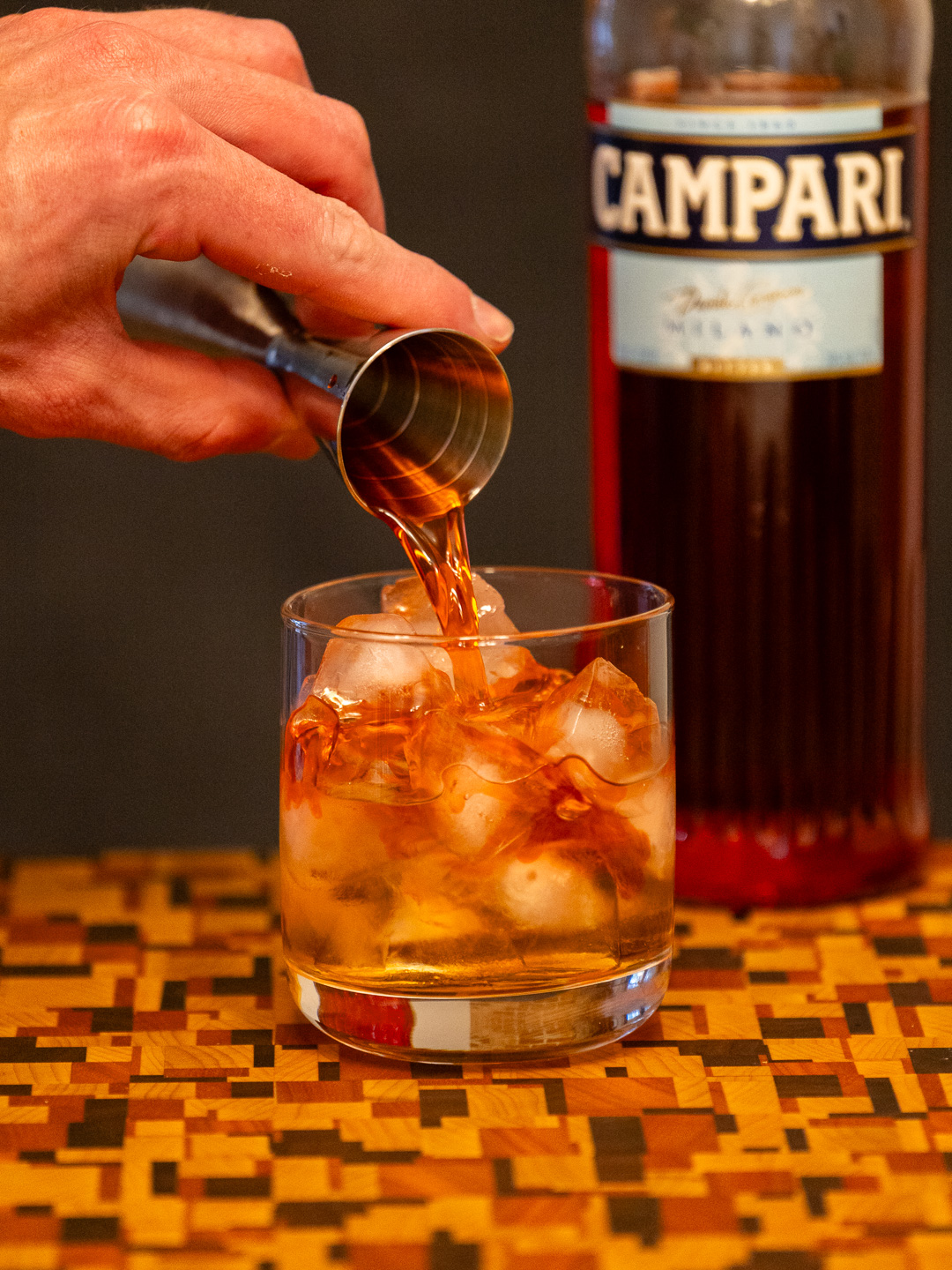 Pouring Campari into a rocks glass filled with ice